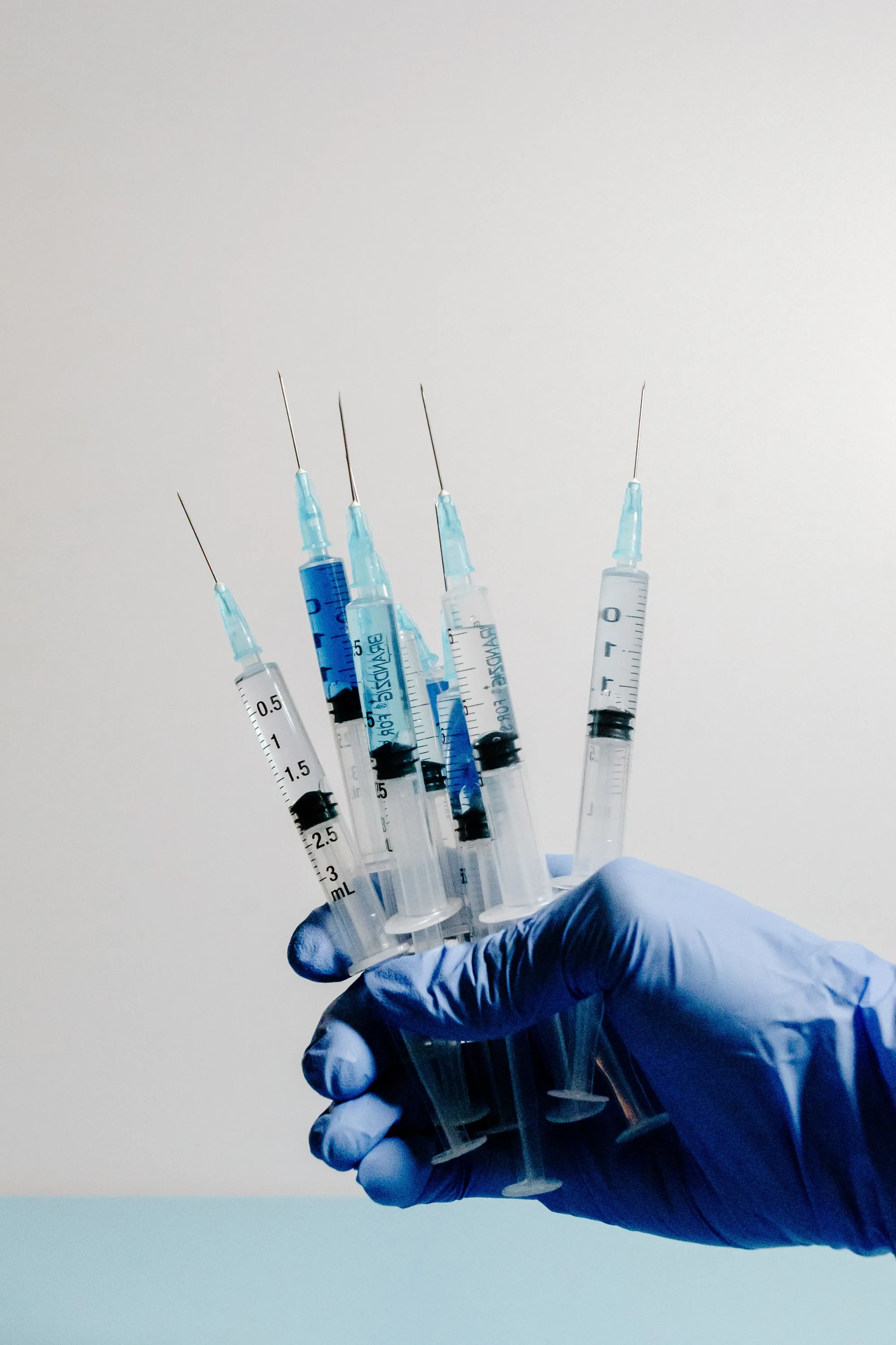A gloved hand holding multiple syringes — the range of injectable treatments available at Novauria Aesthetics.