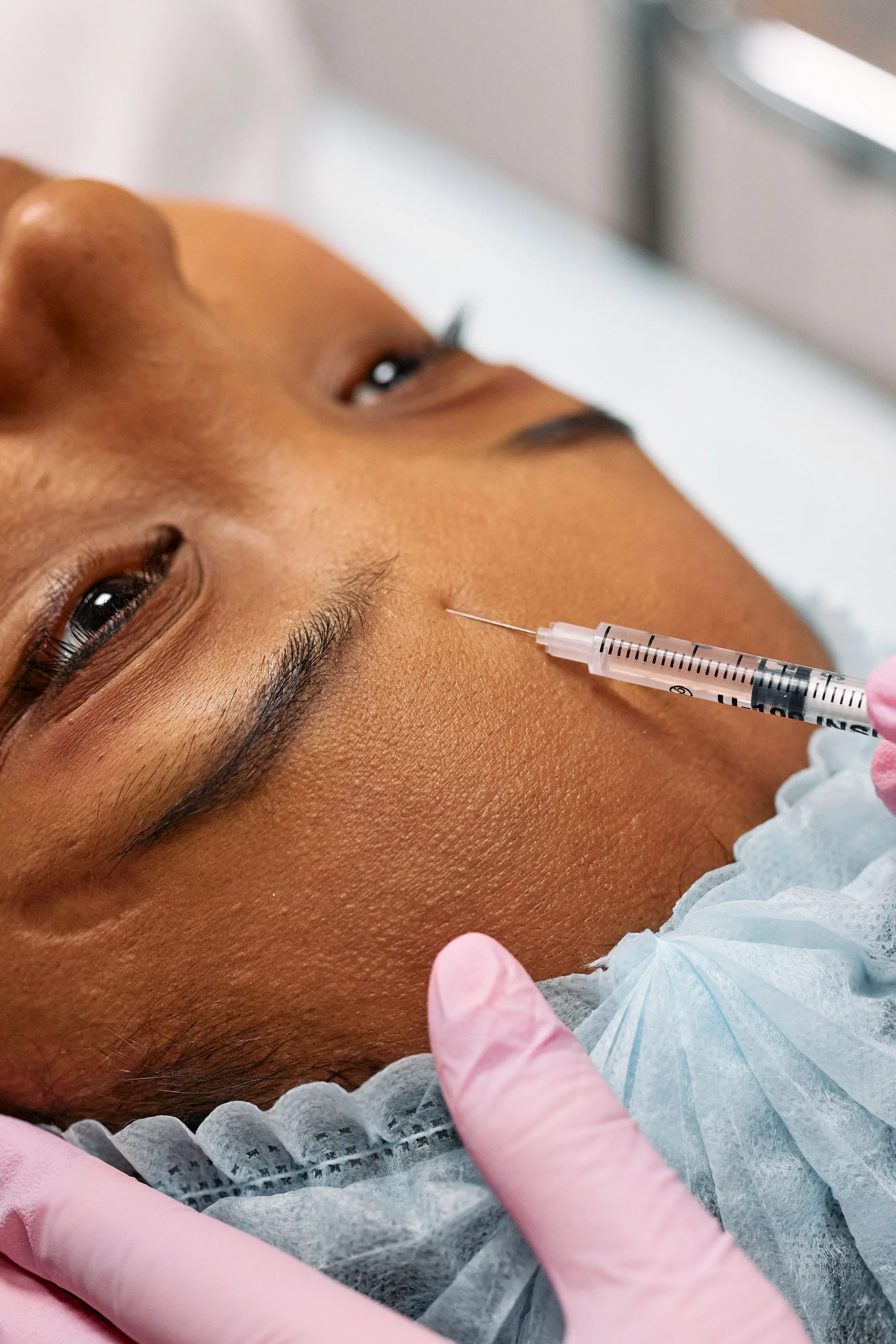 Client receiving an anti-wrinkle injection near the brow, practitioner in pink gloves at Novauria Aesthetics